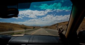 View of cloudy sky and open road through a car windshield 