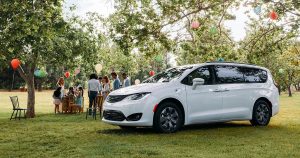 A white 2019 Chrysler Pacifica in the grass with a party going on behind it