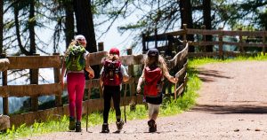 3 children in hiking gear walking down a forest trail.